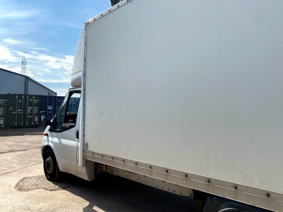 Side view of a white delivery van parked in an industrial area under a clear blue sky.