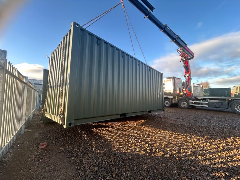 A green shipping container being lifted by a crane in a storage yard.