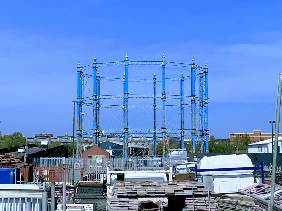 Gas holder structure surrounded by building materials and clear blue sky.