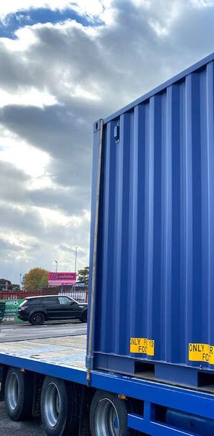 Blue shipping container on a lorry with a cloudy sky in the background.