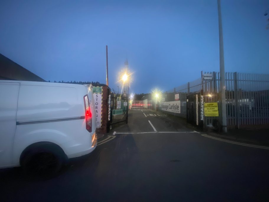 Nighttime view of a gated entrance with a white van and street lights.