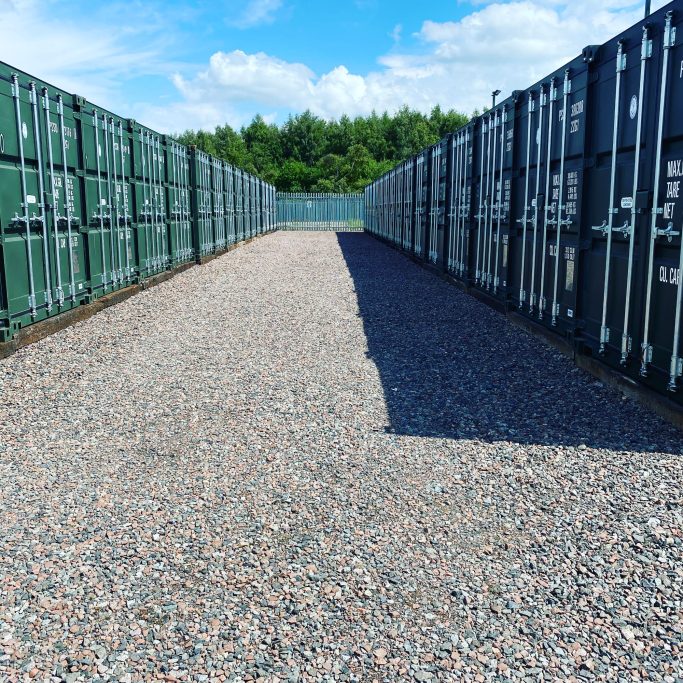 Rows of green storage containers on a gravel surface under a blue sky.