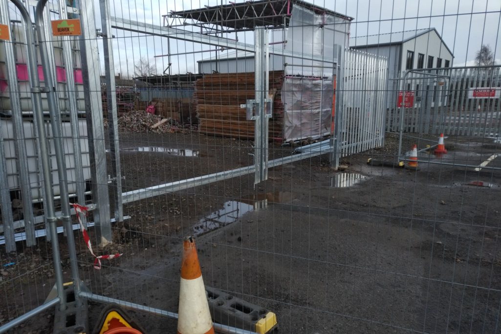Construction site with fencing, scattered materials, and traffic cones.