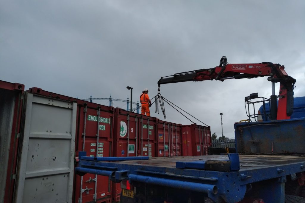 A worker in an orange suit operating a crane over shipping containers.