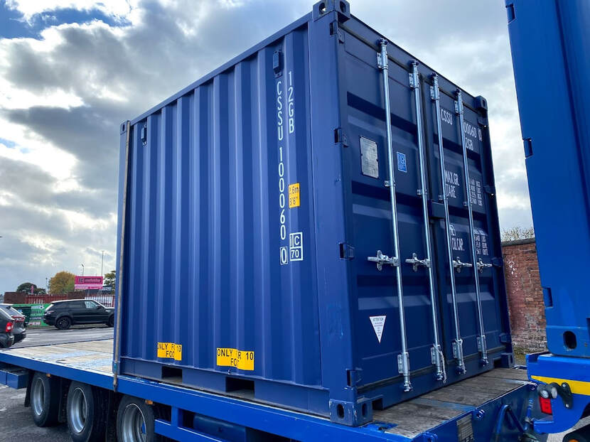 Blue shipping container on a trailer with cloudy sky in the background.