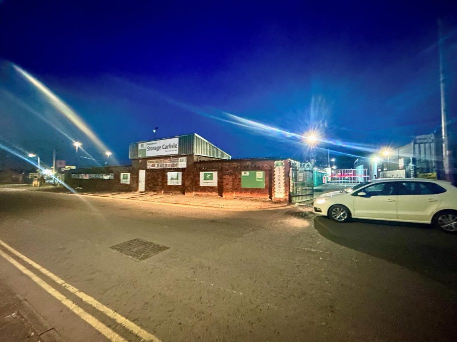 A brightly lit building on a quiet street at night, with a white car parked nearby.