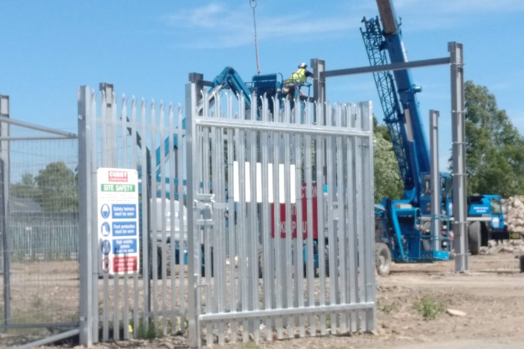 Construction site with a blue crane and worker near a gated entrance.