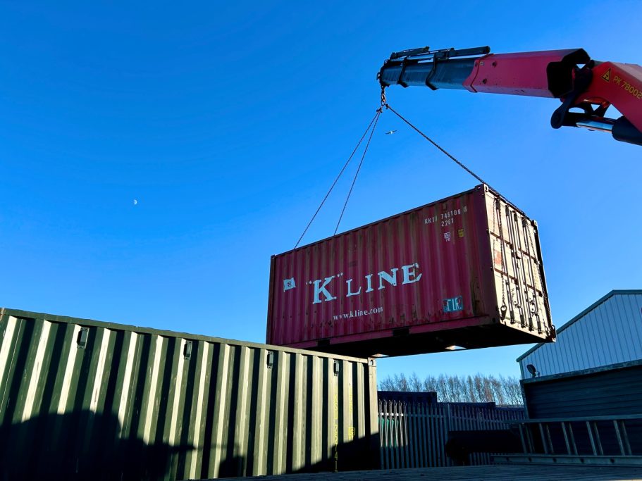 Red shipping container being lifted by a crane against a clear blue sky.