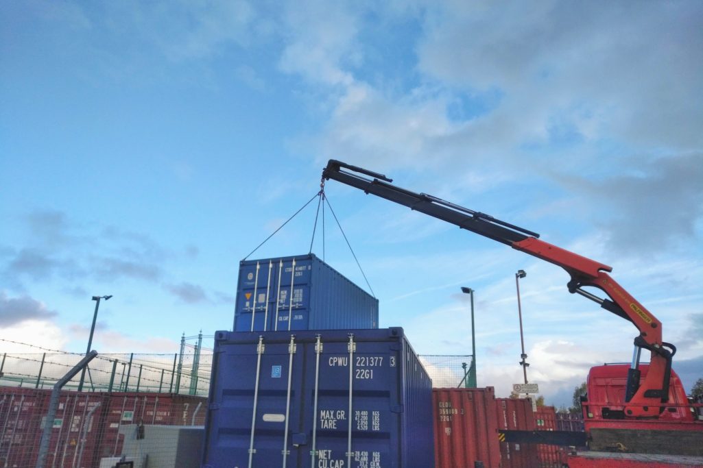 A crane lifting a shipping container against a cloudy sky.
