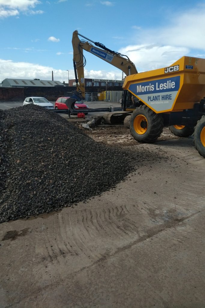 A yellow dumper truck beside a pile of gravel under a blue sky with scattered clouds.