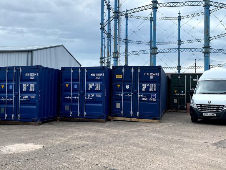 Blue shipping containers lined up next to a gas holder and a white van at Rome Street Depot Carlisle.