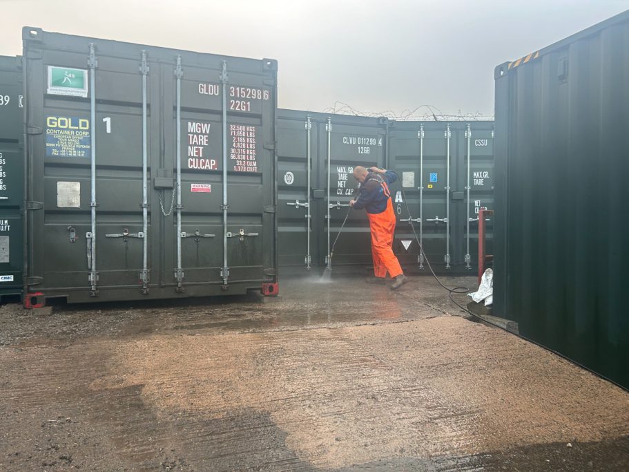 A worker in bright orange overalls operates in a shipping container area.
